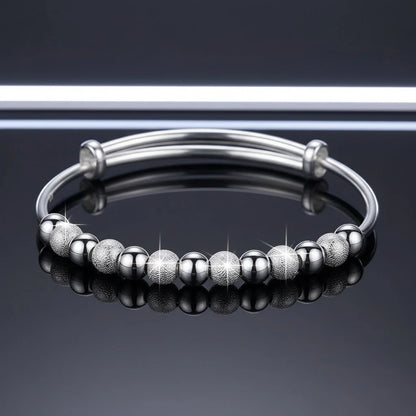 Shiny silver Marvella Beaded Charm Cuff displayed on a glossy black surface, alternating smooth and textured round beads reflecting the studio light in a modern, minimal setting | Oria Jewel