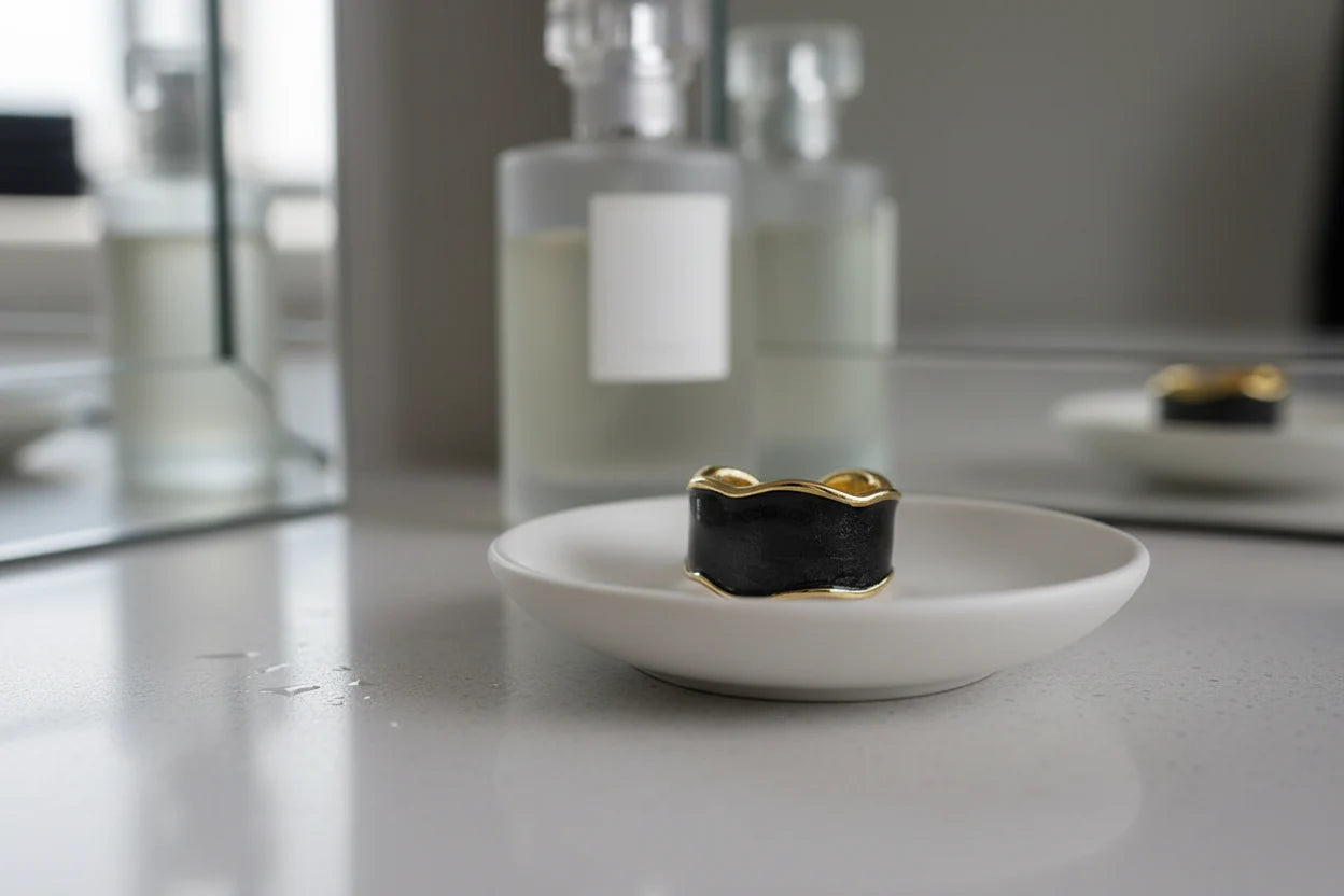 Midnight Black Open Wave Ring displayed on a white ceramic dish beside minimal bottles and a mirror, black open wave band with gold-trim finish | OriaJewel
