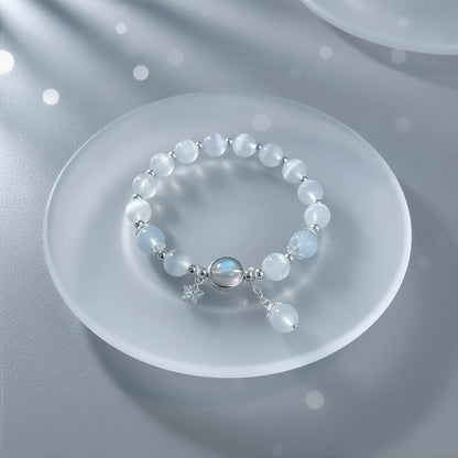 Close-up of Moonstone Glow Charm Bracelet arranged in a circle on a frosted glass plate, highlighting the luminous moonstone center and silver charms | Oria Jewel