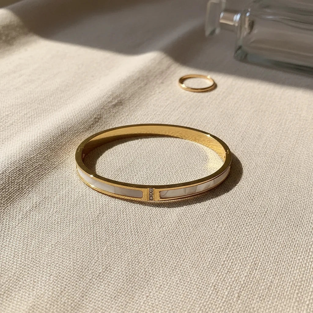 Lifestyle flat-lay of the Mother of Pearl Gold Bangle on soft beige fabric, styled next to a simple gold ring and clear perfume bottle to highlight its refined mother-of-pearl panels and everyday luxury feel | Oria Jewel