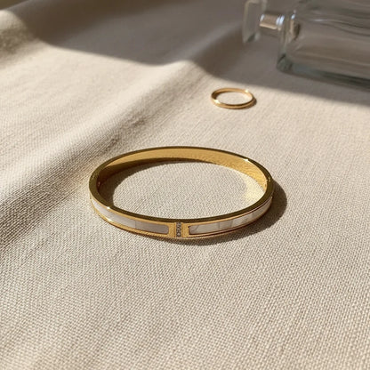 Lifestyle flat-lay of the Mother of Pearl Gold Bangle on soft beige fabric, styled next to a simple gold ring and clear perfume bottle to highlight its refined mother-of-pearl panels and everyday luxury feel | Oria Jewel