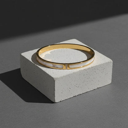 Product shot of the Mother of Pearl Gold Bangle displayed on a gray concrete block, clean shadows and modern background drawing attention to the polished gold finish and luminous inlay | Oria Jewel