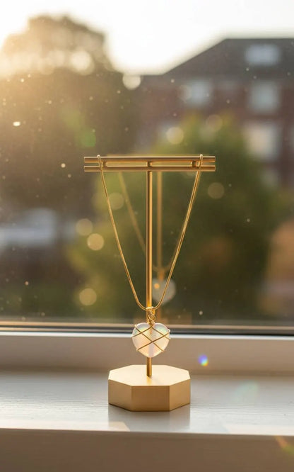 Gold display stand on windowsill holding glowing heart-shaped Natural Moonstone Pendant | Oria Jewel