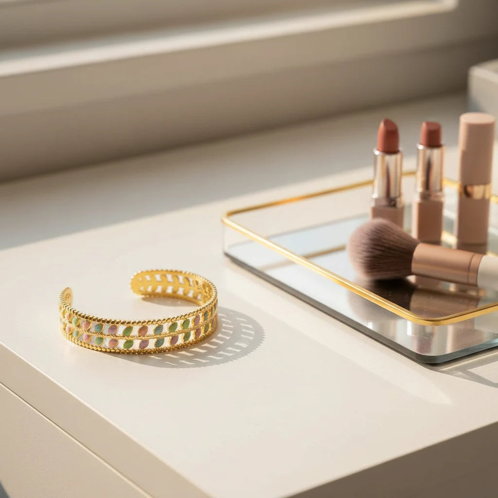 Vanity scene with the Pastel Leaf Garden Cuff Bracelet resting near nude lipsticks and a makeup brush on a mirrored tray, showing the bracelet’s pastel leaf pattern and reflective gold finish in soft morning light | Oria Jewel