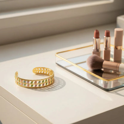 Vanity scene with the Pastel Leaf Garden Cuff Bracelet resting near nude lipsticks and a makeup brush on a mirrored tray, showing the bracelet’s pastel leaf pattern and reflective gold finish in soft morning light | Oria Jewel