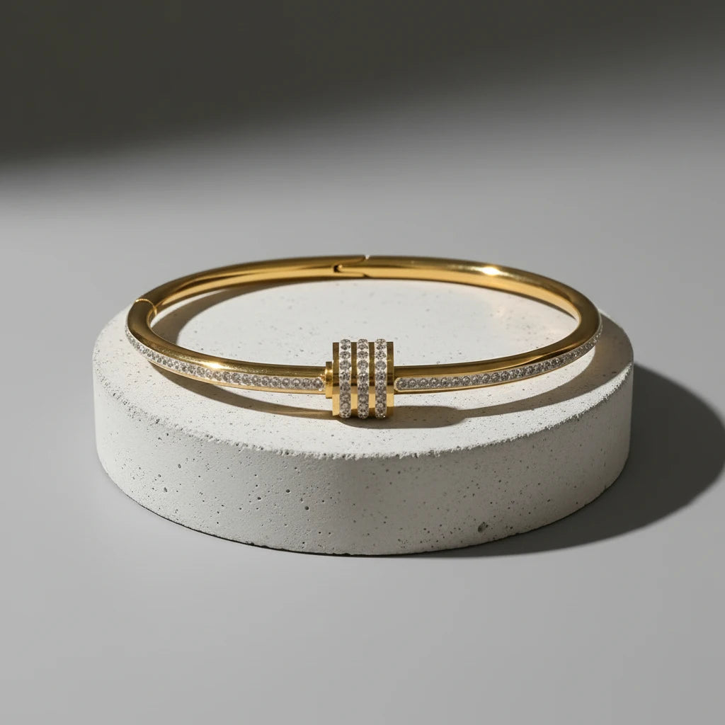 Studio close-up of the Pavé Stackable Gold Bangle displayed on a round concrete pedestal, showcasing its slim gold band and triple pavé crystal center detail under dramatic directional lighting | Oria Jewel