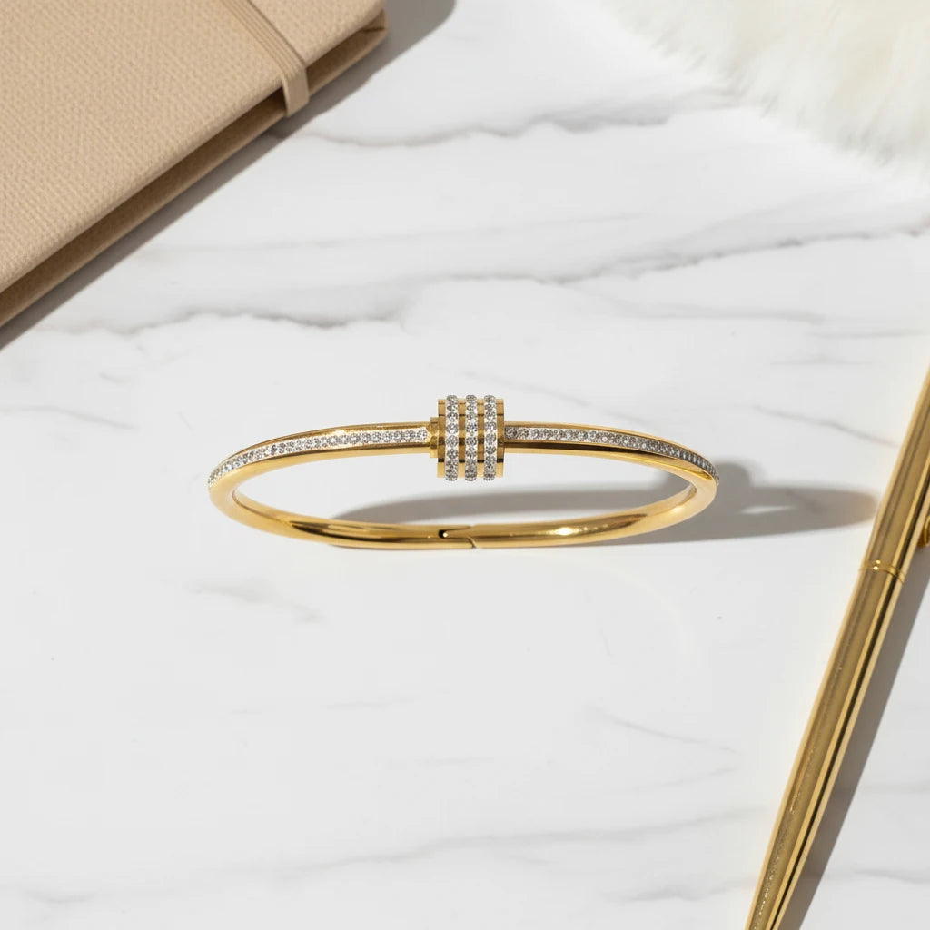 Flat-lay shot of the Pavé Stackable Gold Bangle resting on a white marble surface beside a beige notebook and gold pen, highlighting its sleek pavé-set crystals for an elegant desk-side accessory look | Oria Jewel