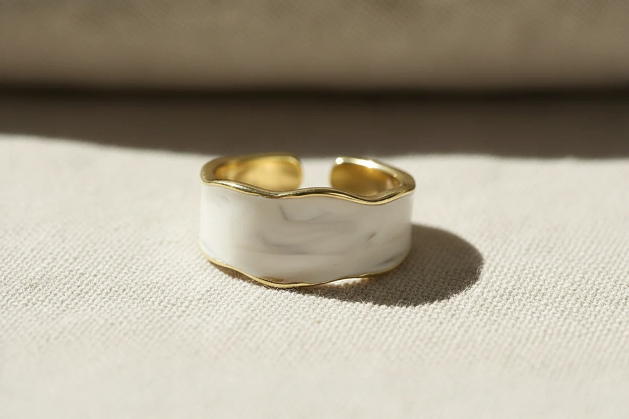Pearl White Open Wave Ring close-up on soft beige fabric in warm sunlight, focusing on the rippled wave silhouette, pearl-like sheen, and thin gold outline around the enamel | OriaJewel