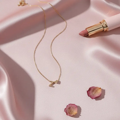 Personalised Heart Necklace Gold with Z initial and tiny heart charm displayed on soft pink satin beside lipstick and rose petals | Oria Jewel