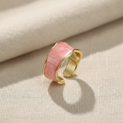 Pink Marble Open Wave Ring close-up on textured cream fabric, showing the glossy pink marbled inlay, gold-tone wavy edges, and adjustable open cuff design in natural light | OriaJewel