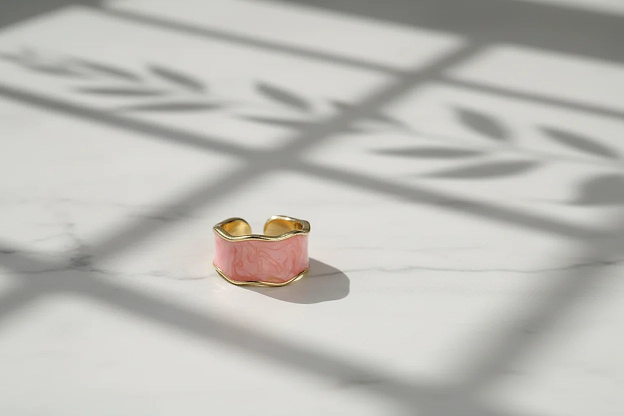 Pink Marble Open Wave Ring on a marble tabletop under window-grid shadows, showcasing the pink marbled finish and gold open edges with crisp natural daylight contrast | OriaJewel
