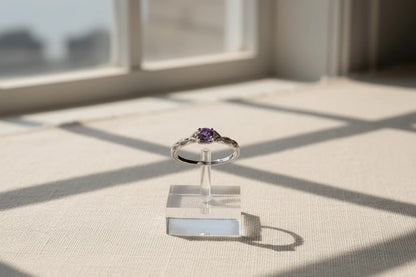 Purple Solitaire Filigree Ring displayed on a clear acrylic stand with bright window-grid shadows on a neutral surface, minimal studio vibe. | OriaJewel