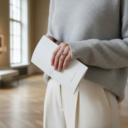 Purple Solitaire Filigree Ring on a hand holding a white booklet in an art gallery, blurred paintings behind, elegant everyday styling. | OriaJewel