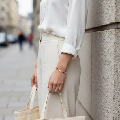 Street-style shot of a woman in an elegant white blouse and tailored cream trousers carrying a tote bag, with the Rainbow Butterfly Pearl Chain Bracelet adding a delicate pop of color and pearls to her wrist | Oria Jewel
