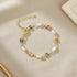 Flat-lay of the Rainbow Butterfly Pearl Chain Bracelet on a soft beige fabric surface, surrounded by stationery items, emphasizing the bracelet’s delicate gold links, alternating pearls, and colorful butterfly charms | Oria Jewel