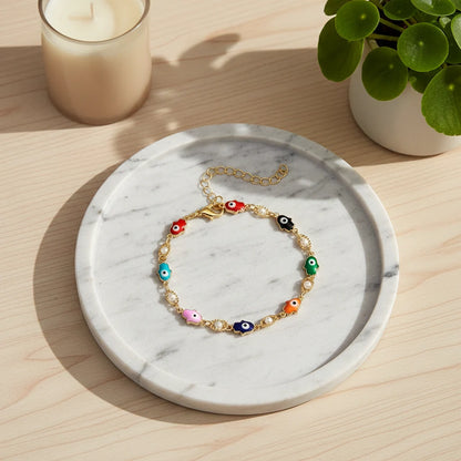 Round marble tray styled with a candle and plant, showcasing the Rainbow Evil Eye Charm Bracelet in a circle, its multicolor charms glowing in natural sunlight | Oria Jewel