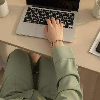 Rainbow Heart Charm Bracelet worn while working on a laptop, vibrant heart charms circling the wrist and catching warm indoor light on a tidy desk | Oria Jewel