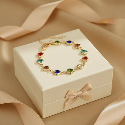 Rainbow Heart Charm Bracelet displayed in a gift box, arranged in a perfect circle of red, blue, green, turquoise and neutral heart charms with satin ribbon props | Oria Jewel