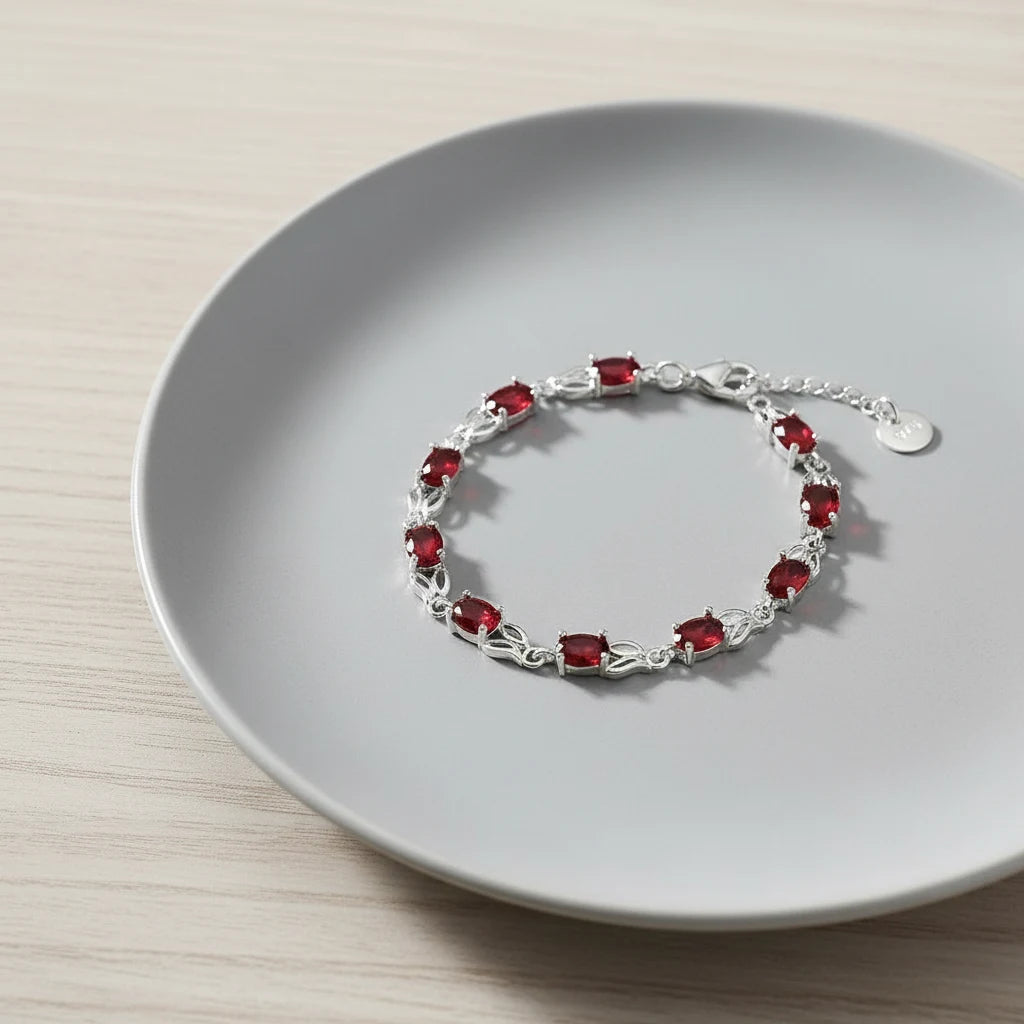 Close-up of the Red Crystal Silver Tennis Bracelet arranged neatly on a soft grey ceramic plate, showing the continuous row of ruby-red crystals framed by slim silver links | Oria Jewel