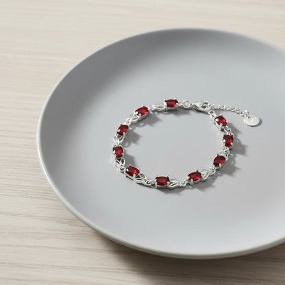 Close-up of the Red Crystal Silver Tennis Bracelet arranged neatly on a soft grey ceramic plate, showing the continuous row of ruby-red crystals framed by slim silver links | Oria Jewel