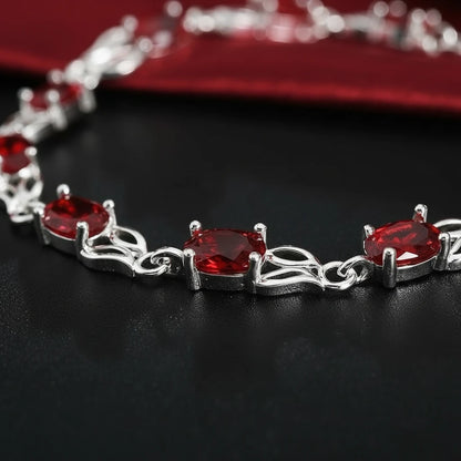 Macro shot of the Red Crystal Silver Tennis Bracelet on a black background, focusing on the faceted red crystals in claw settings and twisted silver links that create a luxurious tennis bracelet style | Oria Jewel