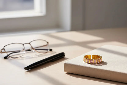 Rose stone band ring on a beige notebook beside glasses and a pen in soft morning sunlight | OriaJewel