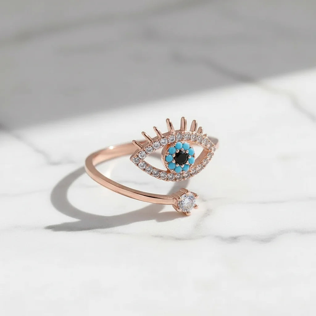Rose Gold Evil Eye Ring on white marble with soft daylight, highlighting the rose-gold open/adjustable design, the evil-eye motif with blue details, and the solitaire-like accent stone | OriaJewel