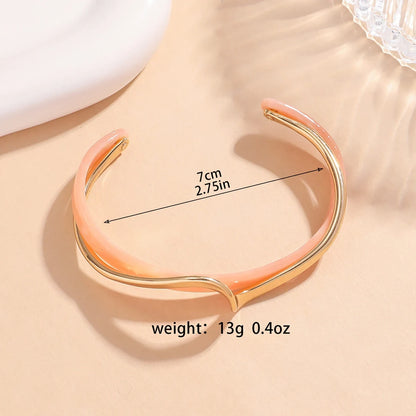 Rosette twist cuff bracelet in blush pink enamel with gold twist detail, shown flat with size 7 cm (2.75 in) and weight 13 g (0.4 oz) text overlay on a soft beige background | Oria Jewel