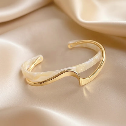 Ivory marbled and gold Rosette twist cuff bracelet displayed on shimmering champagne satin, emphasizing the smooth twisted band and lightweight open-cuff style | Oria Jewel

