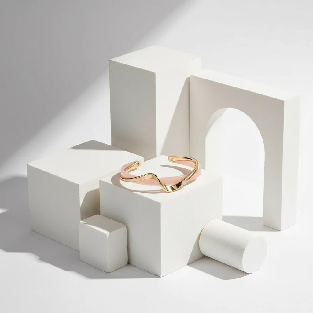 Rosette twist cuff bracelet displayed on modern white geometric blocks, highlighting its sculpted pink band and polished gold twist in a clean studio scene | Oria Jewel