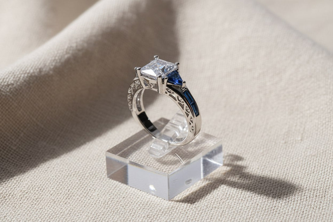Royal Blue Princess Cut Ring close-up on a clear acrylic block over soft beige fabric, detailed side profile showing the square center stone and rich blue triangular side stones | OriaJewel