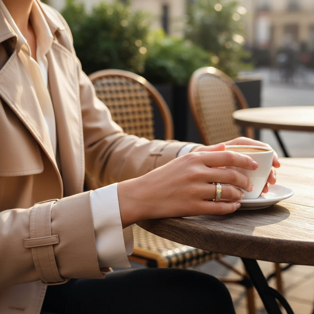 Woman in a beige trench coat holding a coffee cup while wearing a Golden Edge Classic Band ring  | Oria Jewel