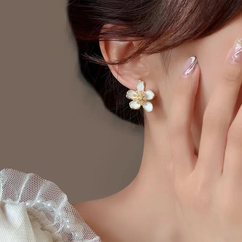 Woman wearing and holding delicate gold-toned flower huggie earrings | Oria Jewel