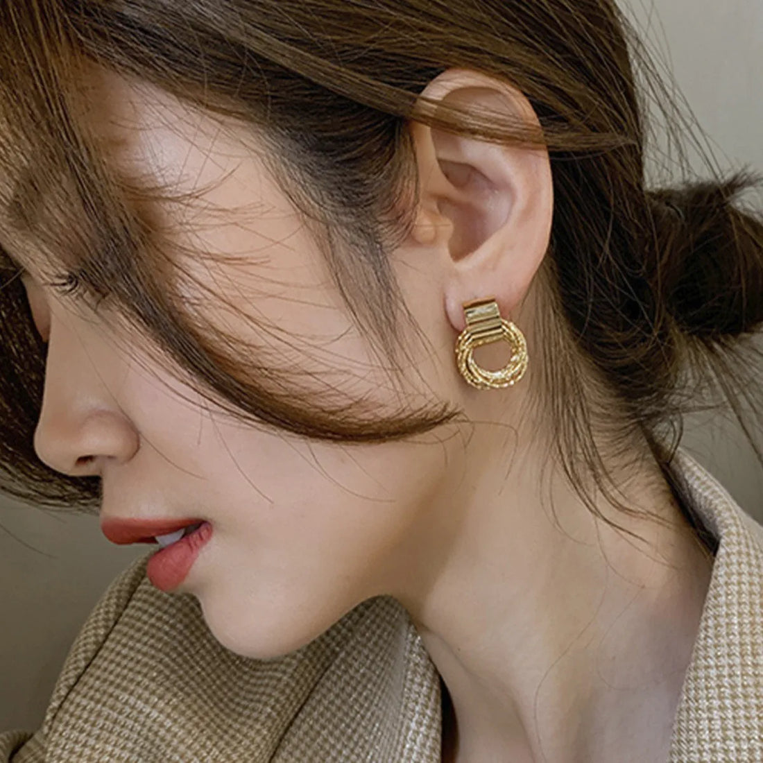 Woman wearing shiny gold knot hoop earrings with intricate braided texture | Oria Jewel