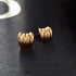 Chunky gold earrings with ribbed design shimmer on dark, textured fabric | Oria Jewel