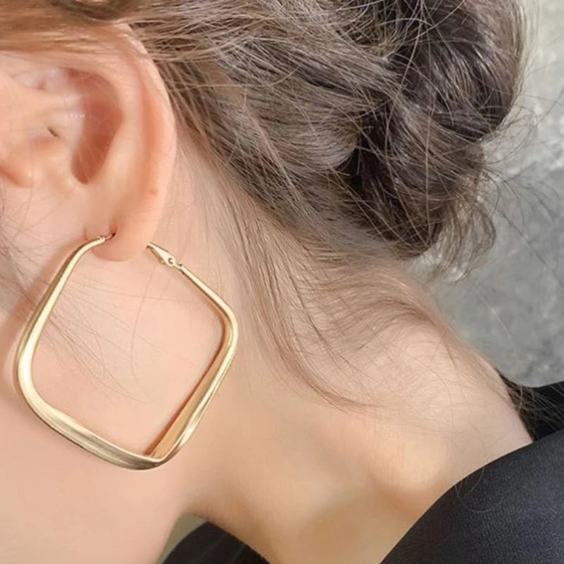 Polished gold diamond shape hoop earrings, one worn on an ear | Oria Jewel