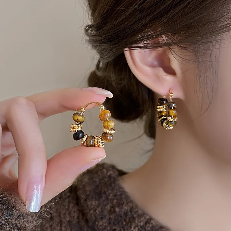 Close-up: hand holds shiny gold Tiger Eye Hoop Earrings, one on ear | Oria Jewel