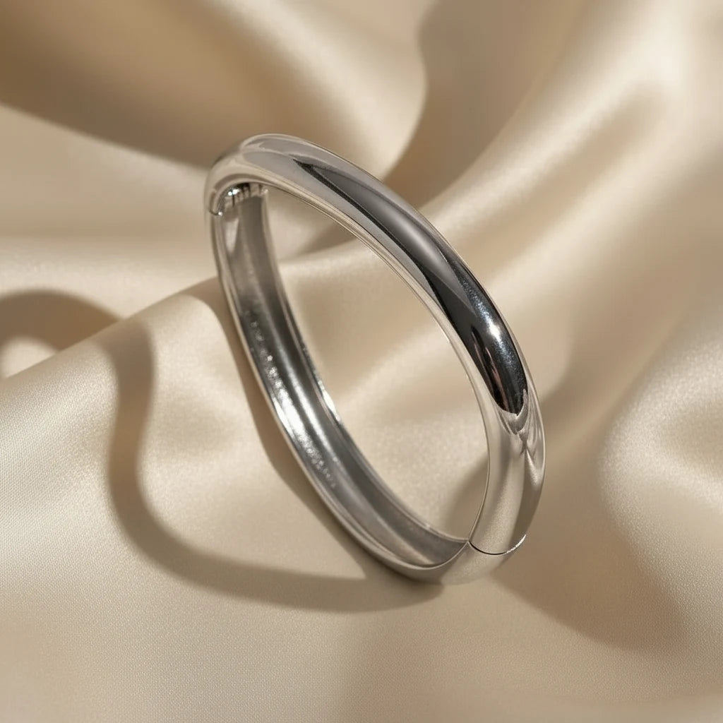 Close-up of the Sculpted Curve Gold Bangle in a cool silver tone on silky fabric, showcasing the same sculpted minimalist design for a modern, versatile accessory option | Oria Jewel