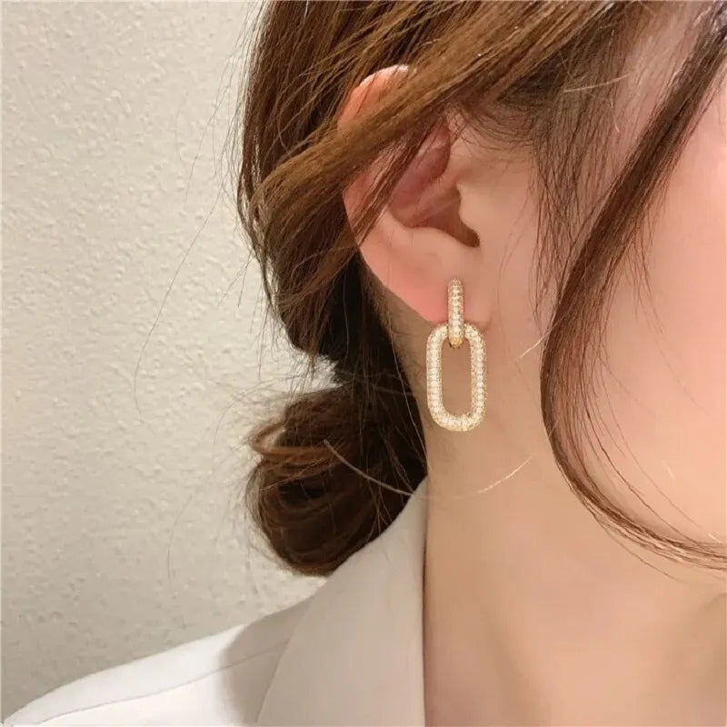 Close-up: Woman wears gold little hoops earring, sparkling pavΓ© rectangular link. | Oria Jewel.
