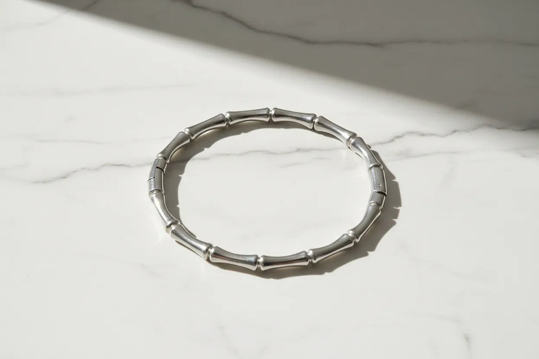 Silver Bamboo bangle Bracelet lying in a neat circle on a white marble surface with soft diagonal sunlight and subtle shadows highlighting each bamboo link | Oria Jewel