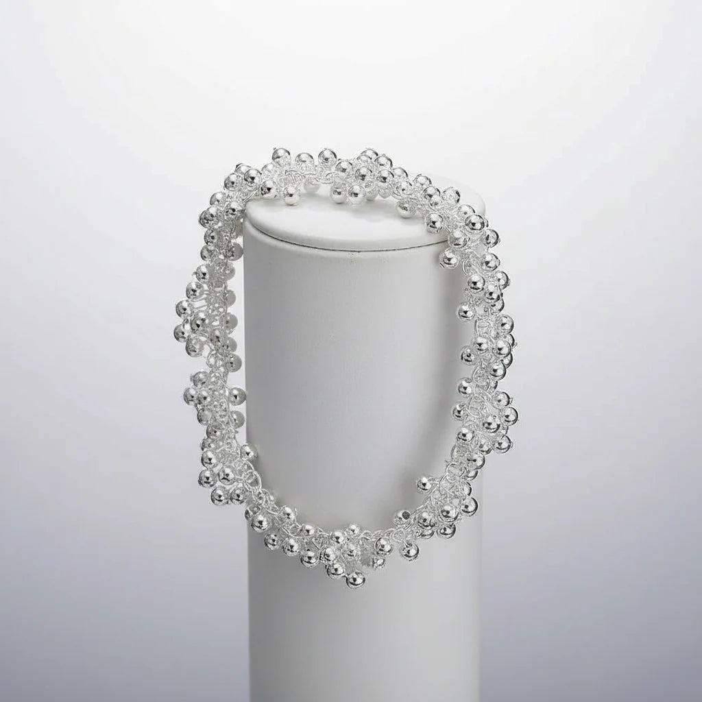 Silver Beaded Cluster Bracelet draped around a white cylindrical display stand against a soft grey background, showing the voluminous bead clusters and dimensional, sparkling silhouette | Oria Jewel