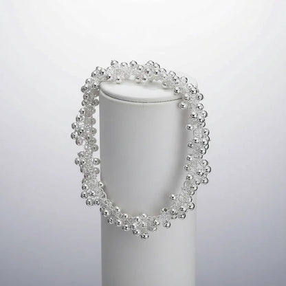Silver Beaded Cluster Bracelet draped around a white cylindrical display stand against a soft grey background, showing the voluminous bead clusters and dimensional, sparkling silhouette | Oria Jewel