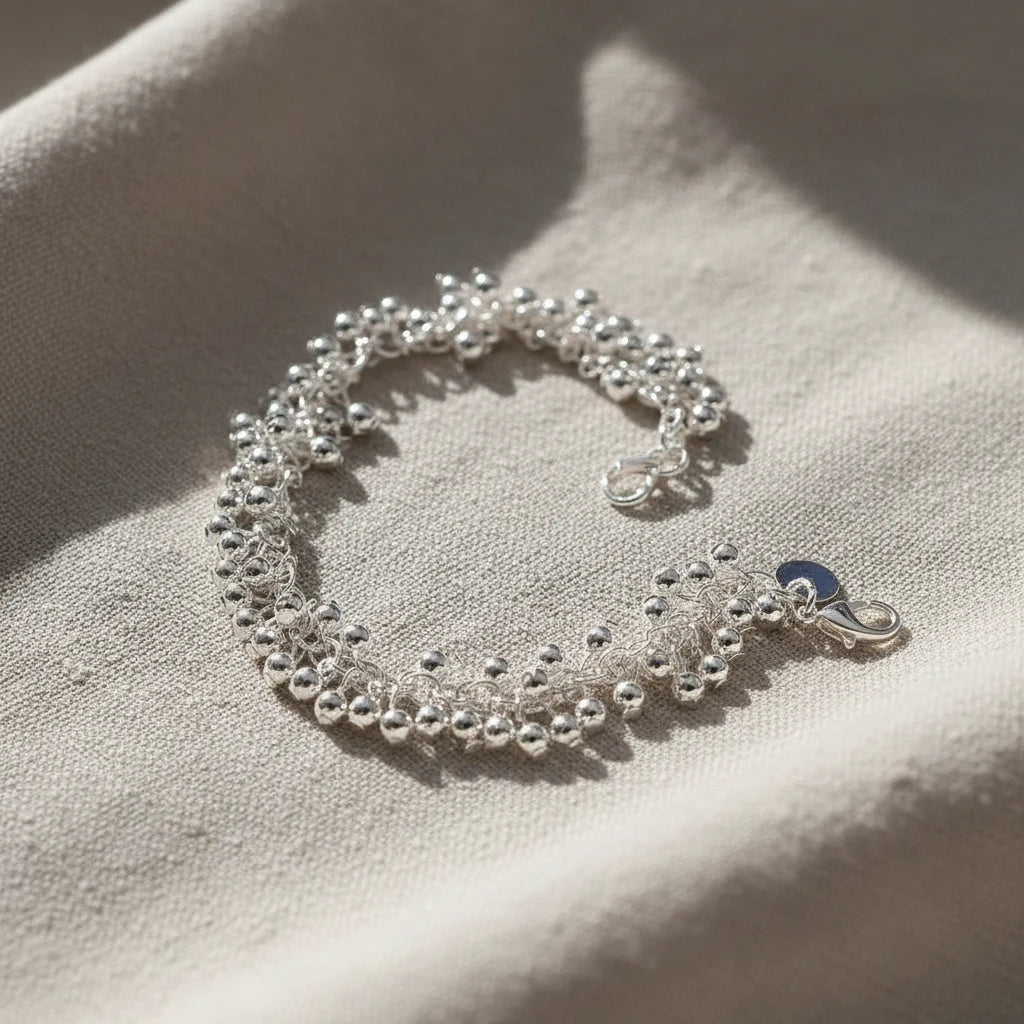 Silver Beaded Cluster Bracelet styled on a beige fabric surface in natural sunlight, capturing the shimmer of the silver beads and the soft, elegant drape of the bracelet | Oria Jewel