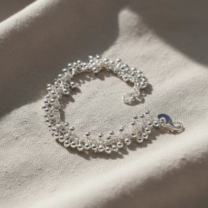 Silver Beaded Cluster Bracelet styled on a beige fabric surface in natural sunlight, capturing the shimmer of the silver beads and the soft, elegant drape of the bracelet | Oria Jewel
