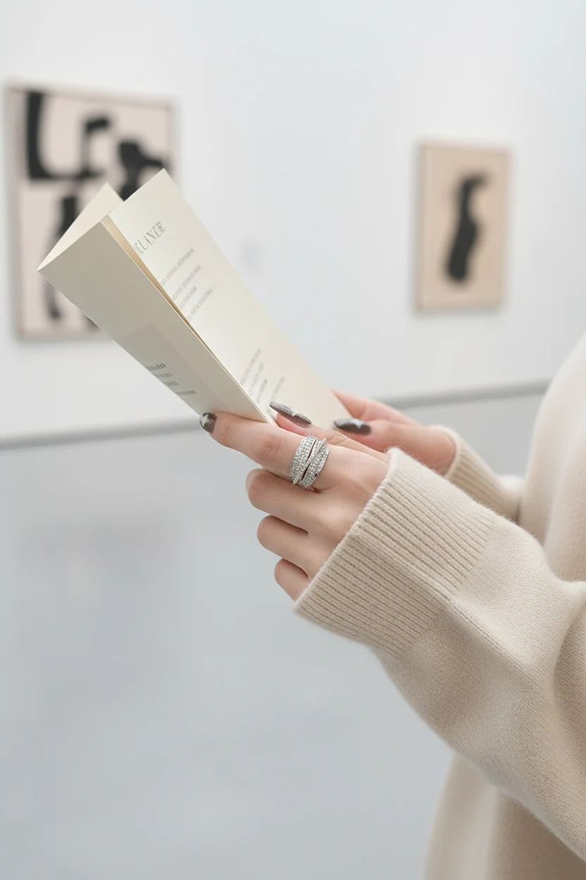 Silver CZ Wrap Ring worn on a hand holding a booklet in a minimal art-gallery scene, highlighting the multi-row wrap design and bright CZ shine | OriaJewel