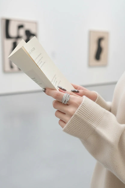 Silver CZ Wrap Ring worn on a hand holding a booklet in a minimal art-gallery scene, highlighting the multi-row wrap design and bright CZ shine | OriaJewel