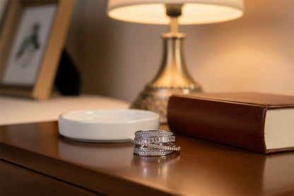 Silver CZ Wrap Ring styled on a wooden tabletop beside a lamp and book, warm cozy lighting showcasing the pavé CZ bands and baguette center line | OriaJewel