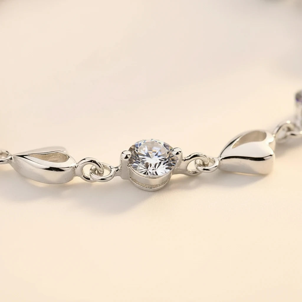 Close-up macro shot of a single round crystal link and adjoining heart-shaped links from the Silver Heart Crystal Tennis Bracelet, showcasing the brilliant faceting, polished silver finish, and fine craftsmanship against a warm beige background | Oria Jewel