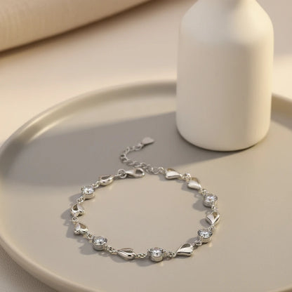 Soft beige tabletop scene featuring the Silver Heart Crystal Tennis Bracelet laid on a round tray next to a matte white vase, emphasizing the bracelet’s continuous row of glittering crystals and petite silver heart charms | Oria Jewel