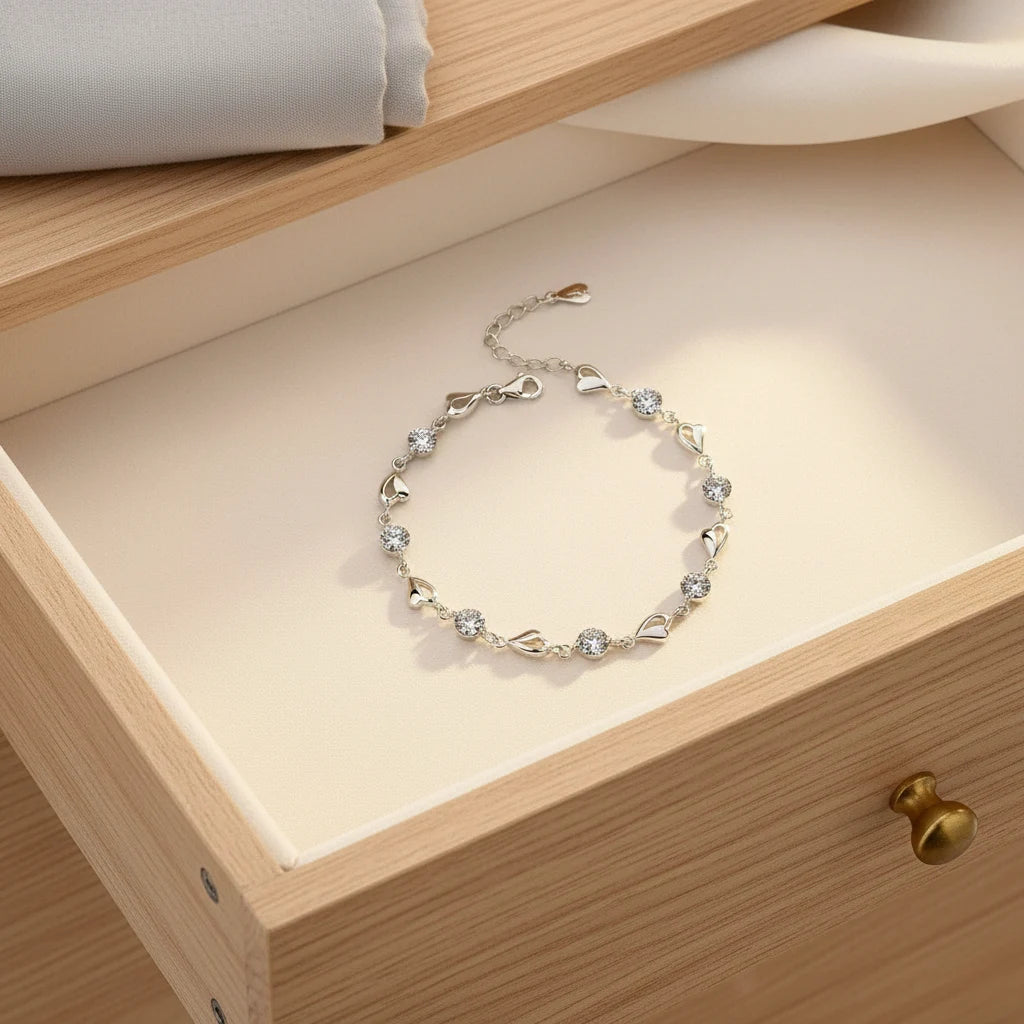 Drawer flat-lay of the Silver Heart Crystal Tennis Bracelet arranged neatly inside a wooden jewelry drawer, with folded fabric nearby, highlighting the elegant design and luxe sparkle of the silver hearts and crystal stones | Oria Jewel